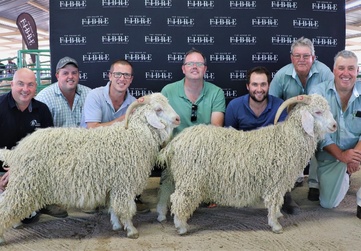 Group of individuals posing with two Angora goats at an agricultural event, standing in front of a banner with repeated House of Fibre logos.