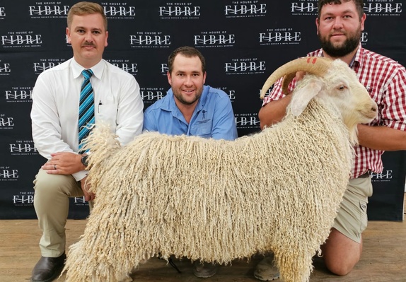 Three individuals posing with a prize-winning Angora goat at an event hosted by House of Fibre.