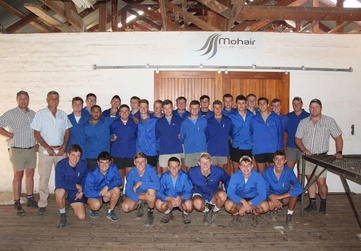 Group of individuals from Landbouskool Marlow, in blue shirts posing for a photo in front of a Mohair sign in a rustic indoor setting.