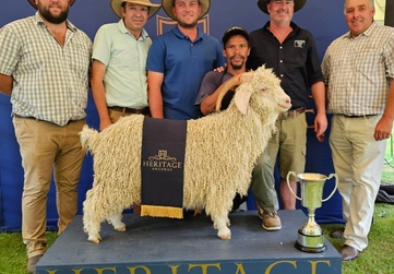 Group of five individuals posing with a champion angora goat at a livestock show, standing under a tent with a banner reading 